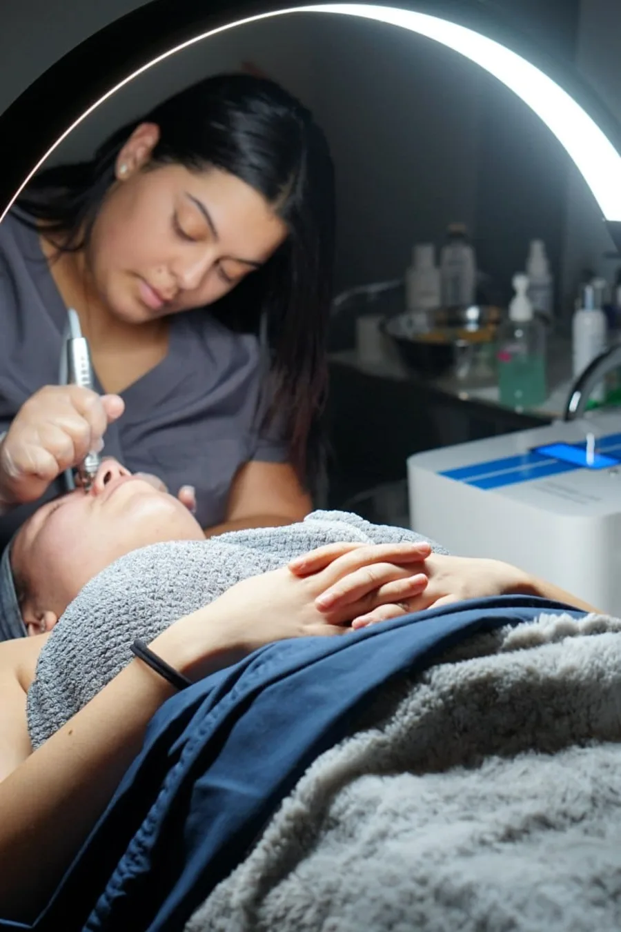 A licensed esthetician performing a facial treatment under a ring light at Faciallash Lounge in Fort Myers